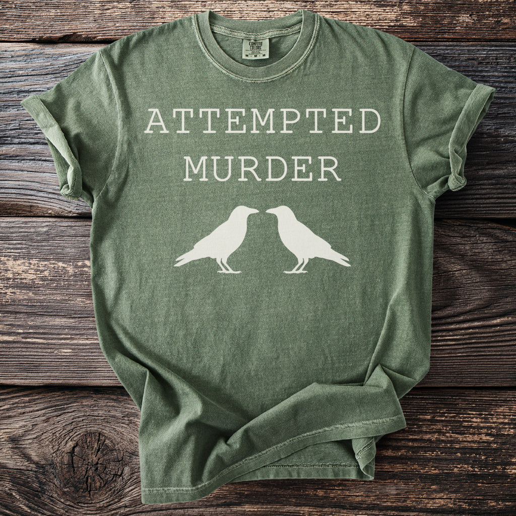 Green t-shirt with "ATTEMPTED MURDER" and two white bird silhouettes.