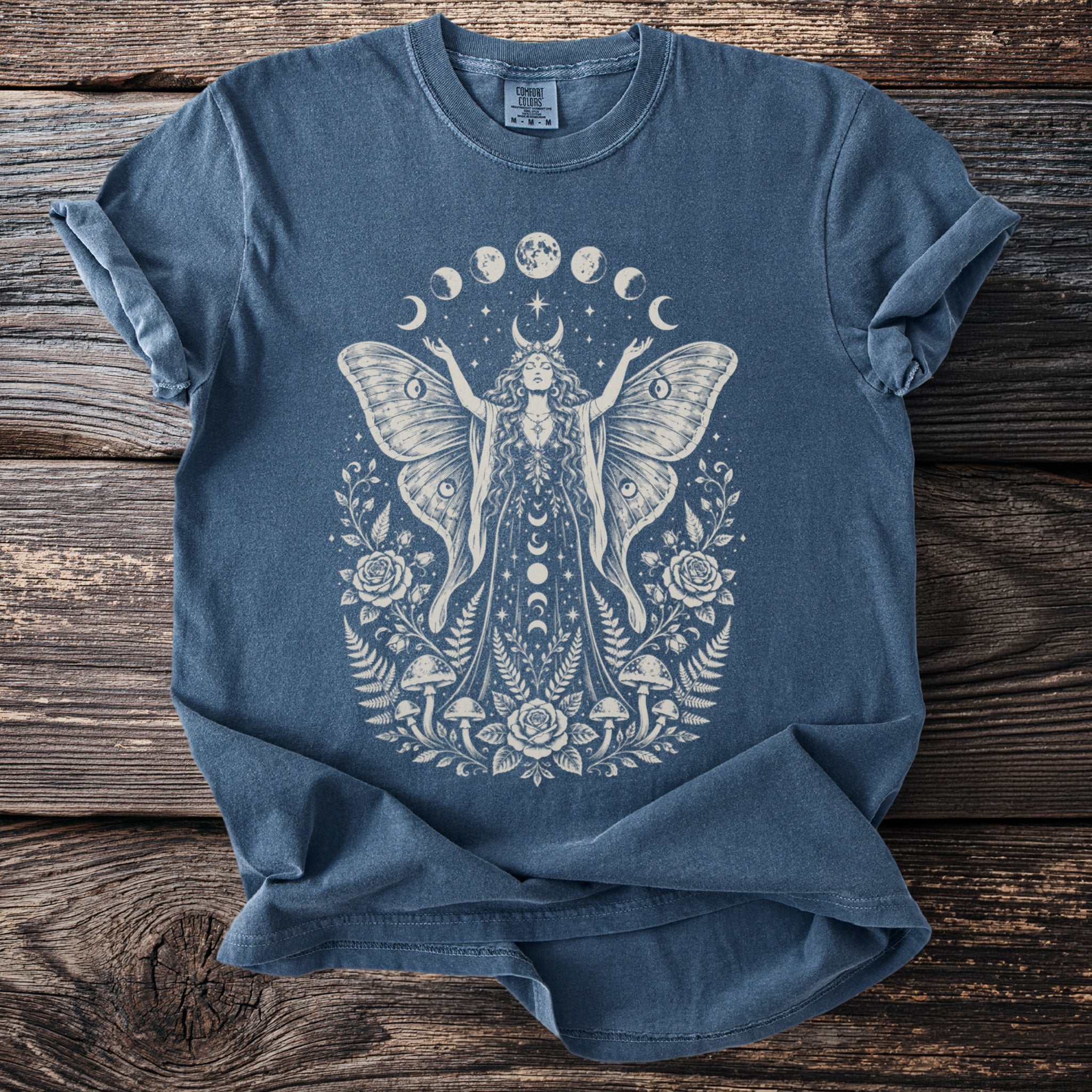 Blue t-shirt with cream moth woman, moon phases, roses, mushrooms, and ferns graphic.