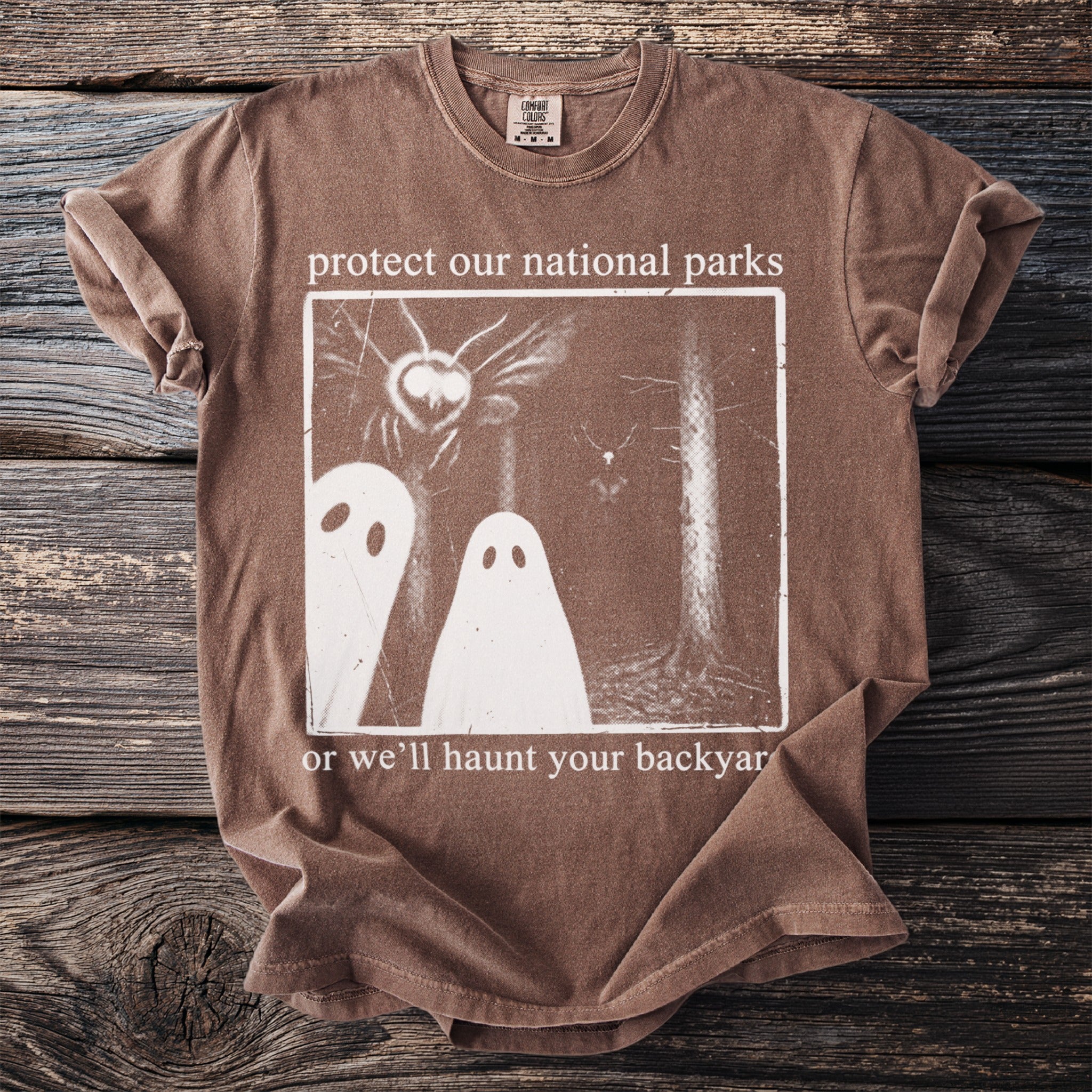 Brown t-shirt with graphic and text "protect our national parks or we'll haunt your backyard".