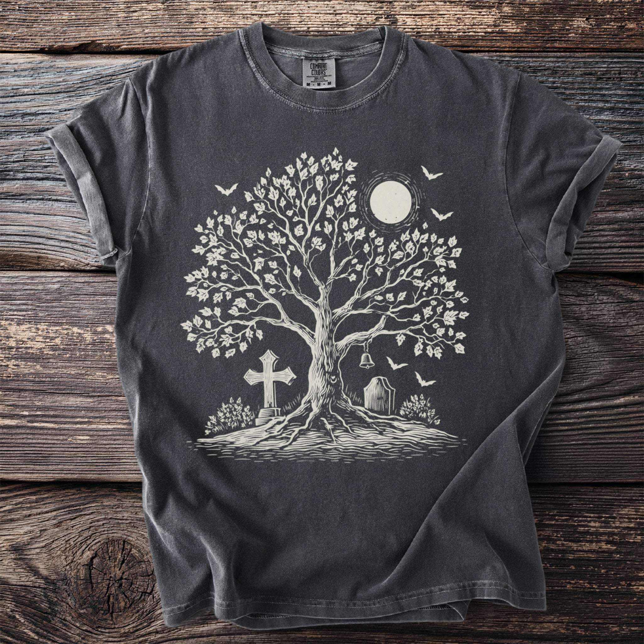 Dark grey t-shirt with a white graphic of a tree, moon, cross, tombstone, bell, and birds.