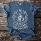 Blue t-shirt with circular nature-themed graphic of a goddess, plants, moon phases, and candles.
