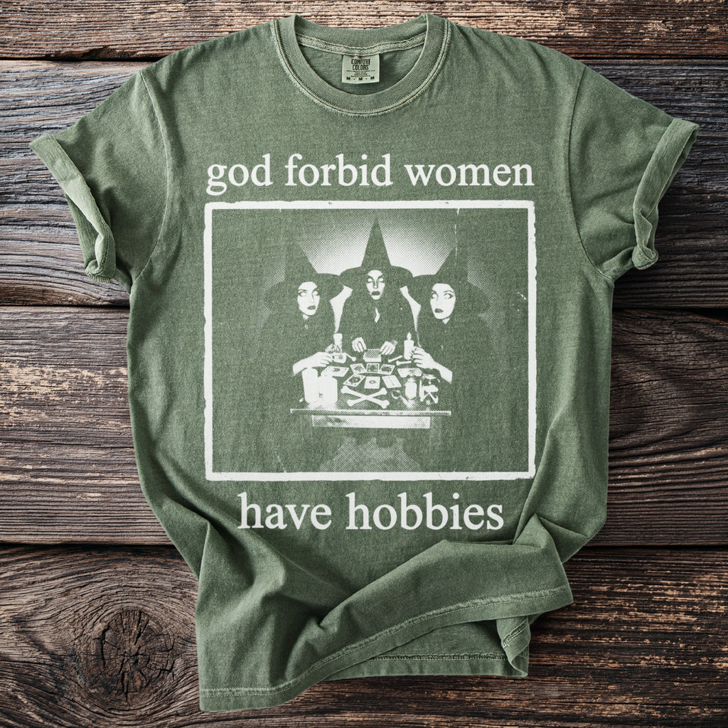Green t-shirt with "god forbid women have hobbies" text and a graphic of three witches.