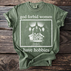 Green t-shirt with "god forbid women have hobbies" text and a graphic of three witches.