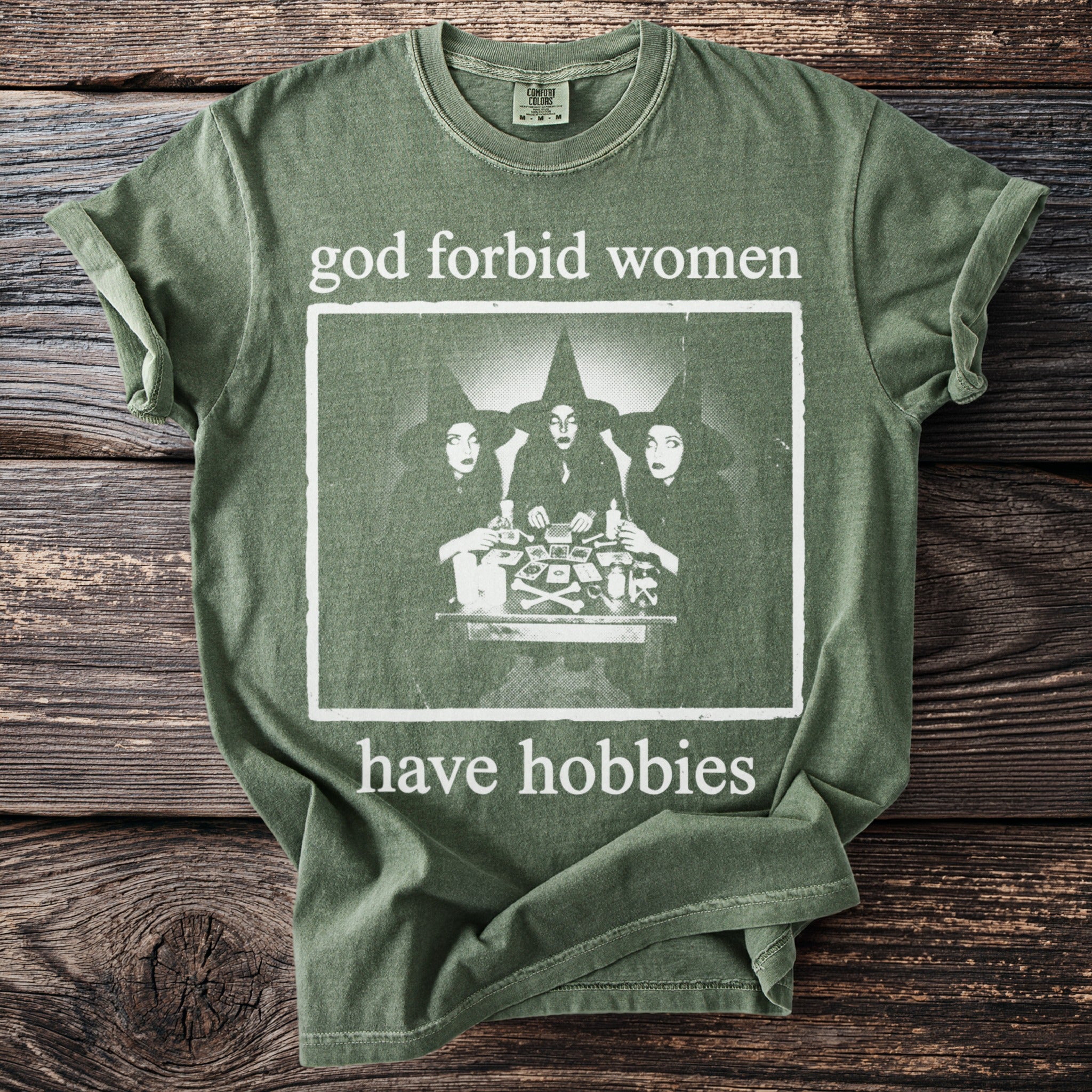 Green t-shirt with "god forbid women have hobbies" text and a graphic of three witches.