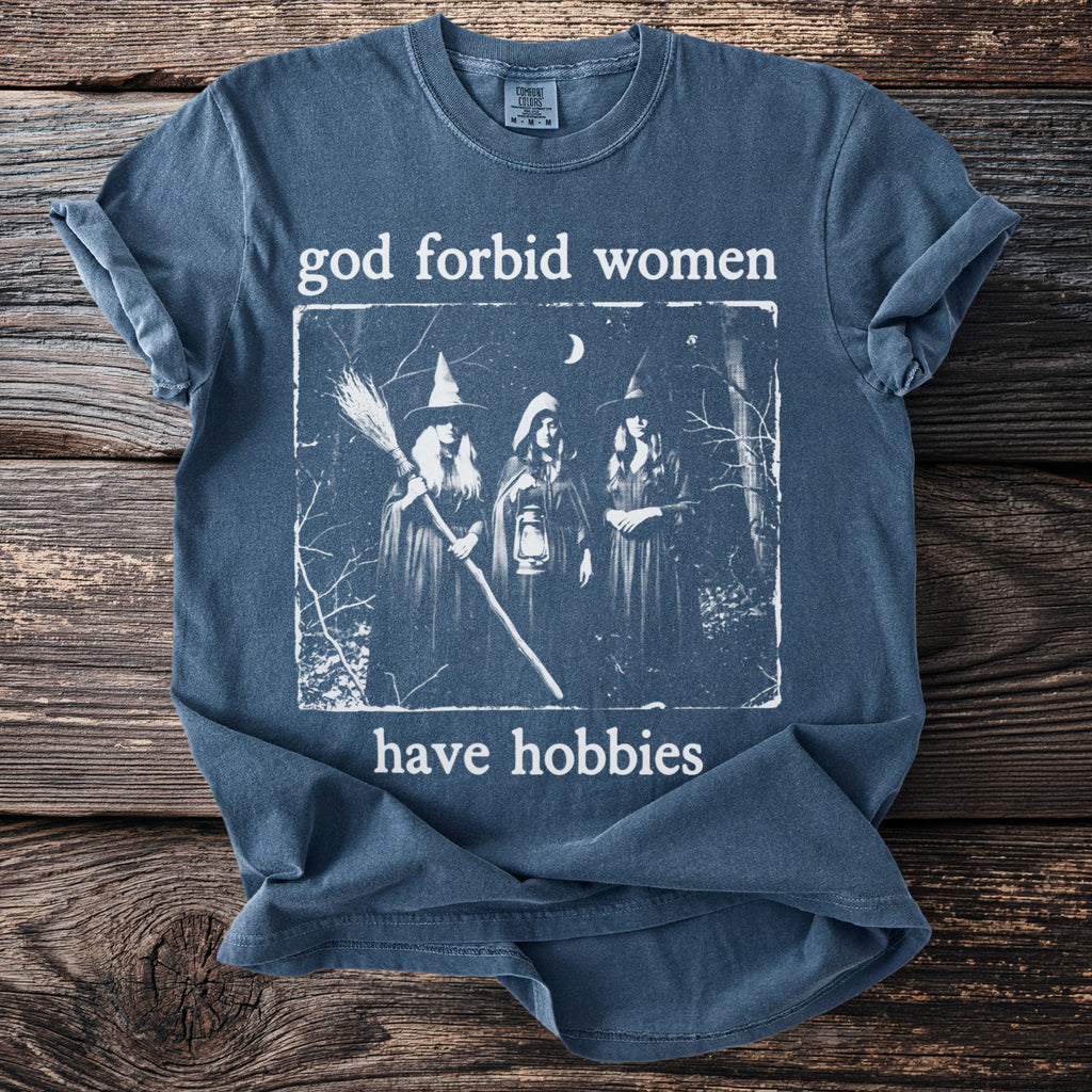 Blue t-shirt with graphic text "god forbid women have hobbies" and three witches.