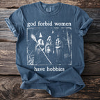 Blue t-shirt with graphic text "god forbid women have hobbies" and three witches.