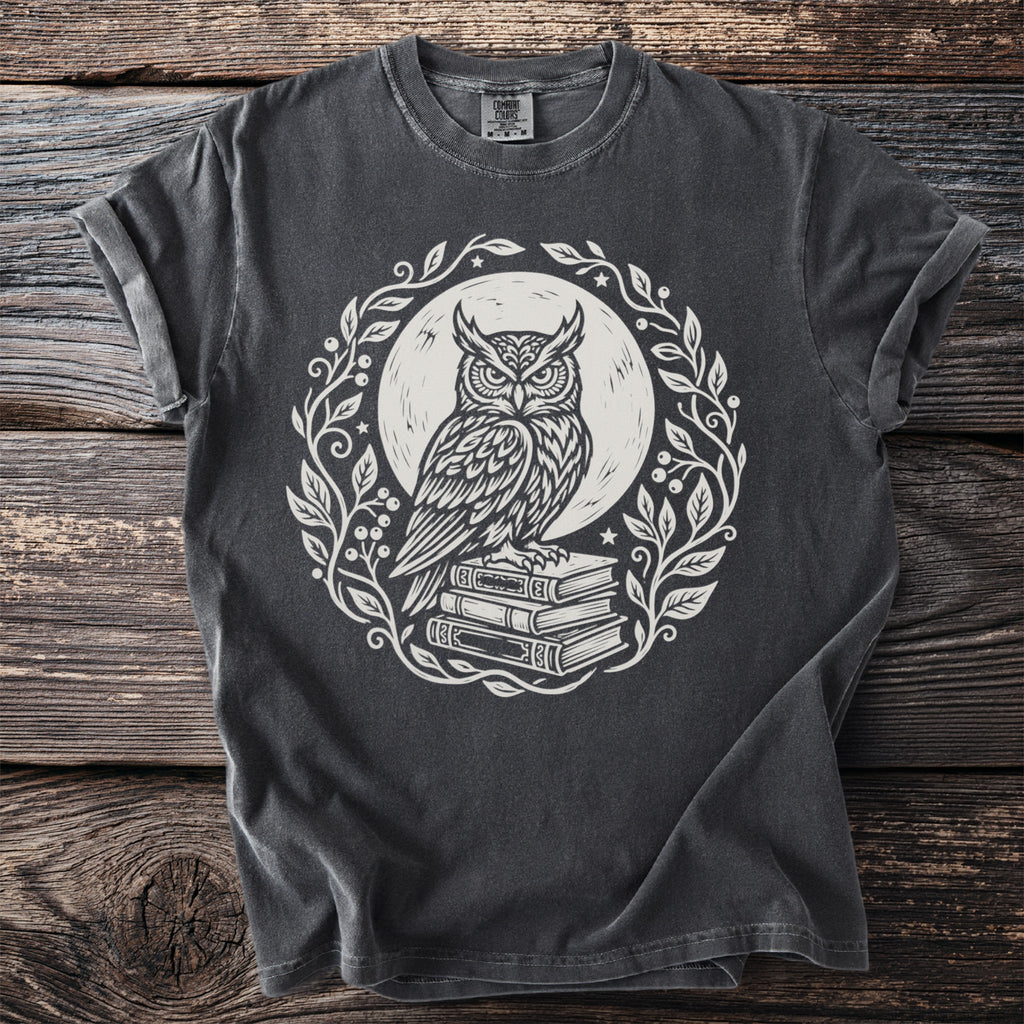 Dark gray t-shirt with white linocut print of owl on books within floral wreath.