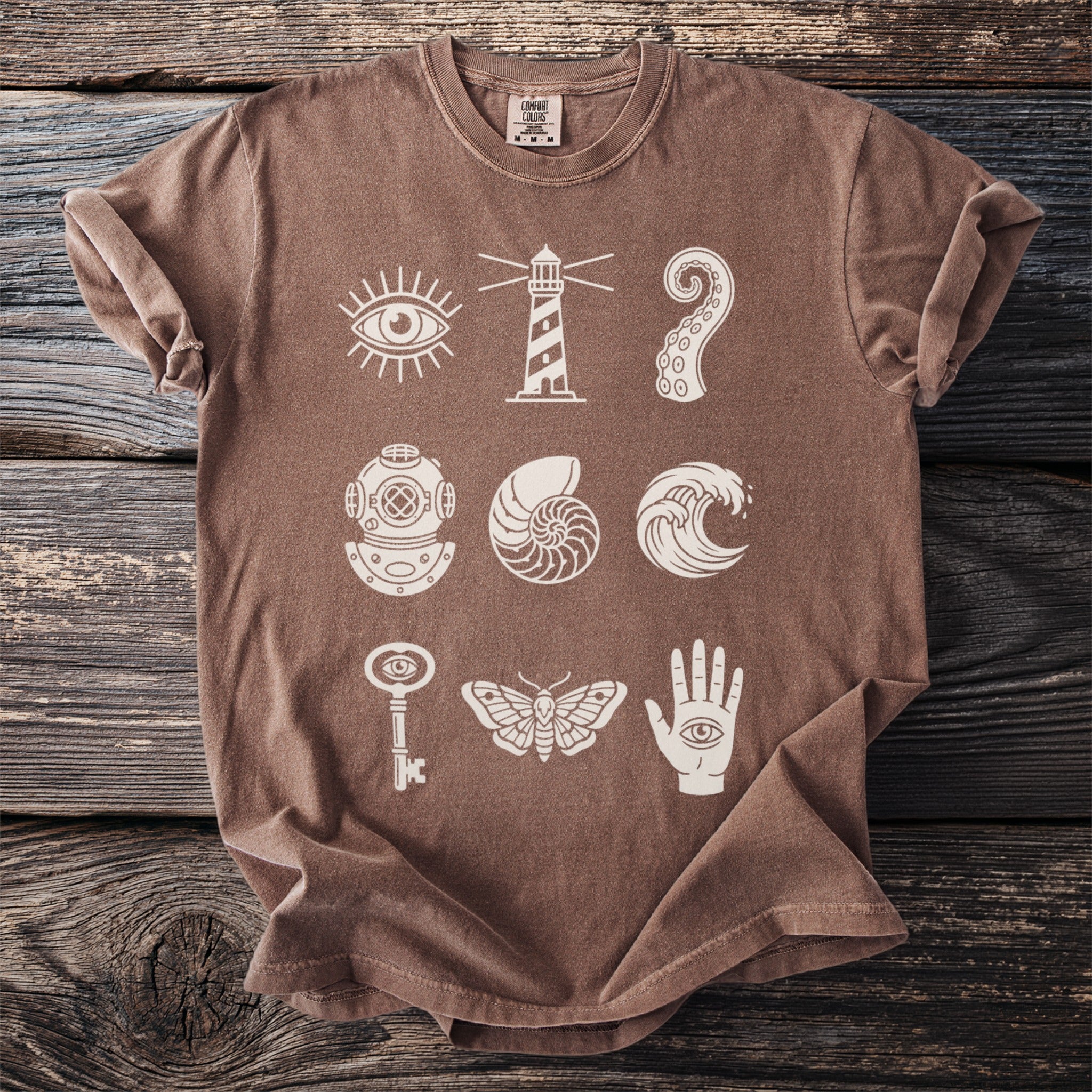 Brown t-shirt with white mystical and nautical graphics arranged in a grid.