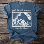 Blue t-shirt with "god forbid women have hobbies" text and a dark graphic.