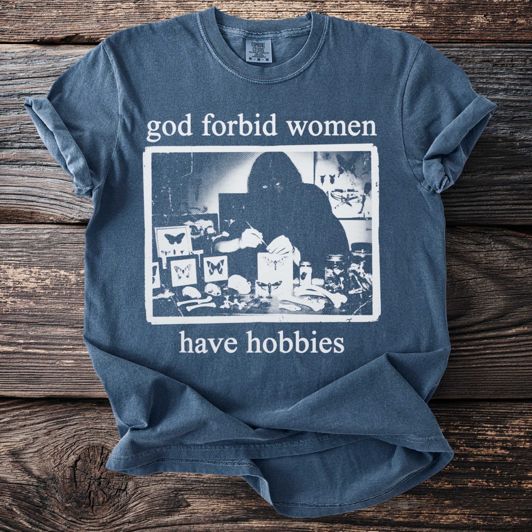 Blue t-shirt with "god forbid women have hobbies" text and a dark graphic.