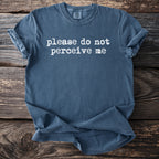 Blue t-shirt with white text "please do not perceive me" on wooden background.