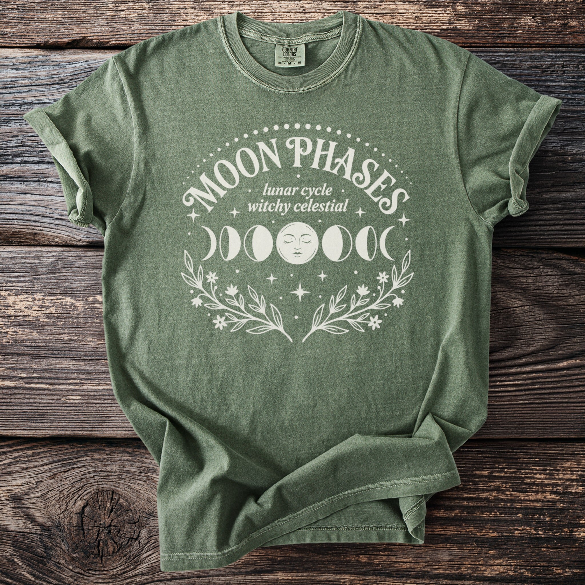 Green t-shirt with "Moon Phases lunar cycle witchy celestial" text and moon graphics.