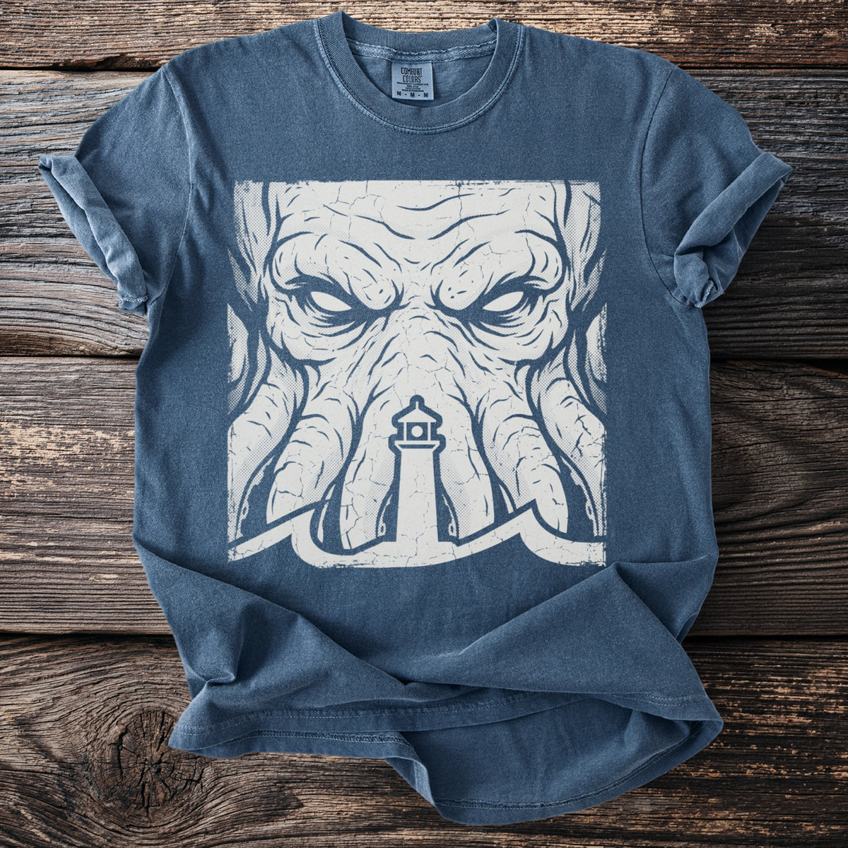 Blue t-shirt with a distressed graphic of a kraken's face and a lighthouse.