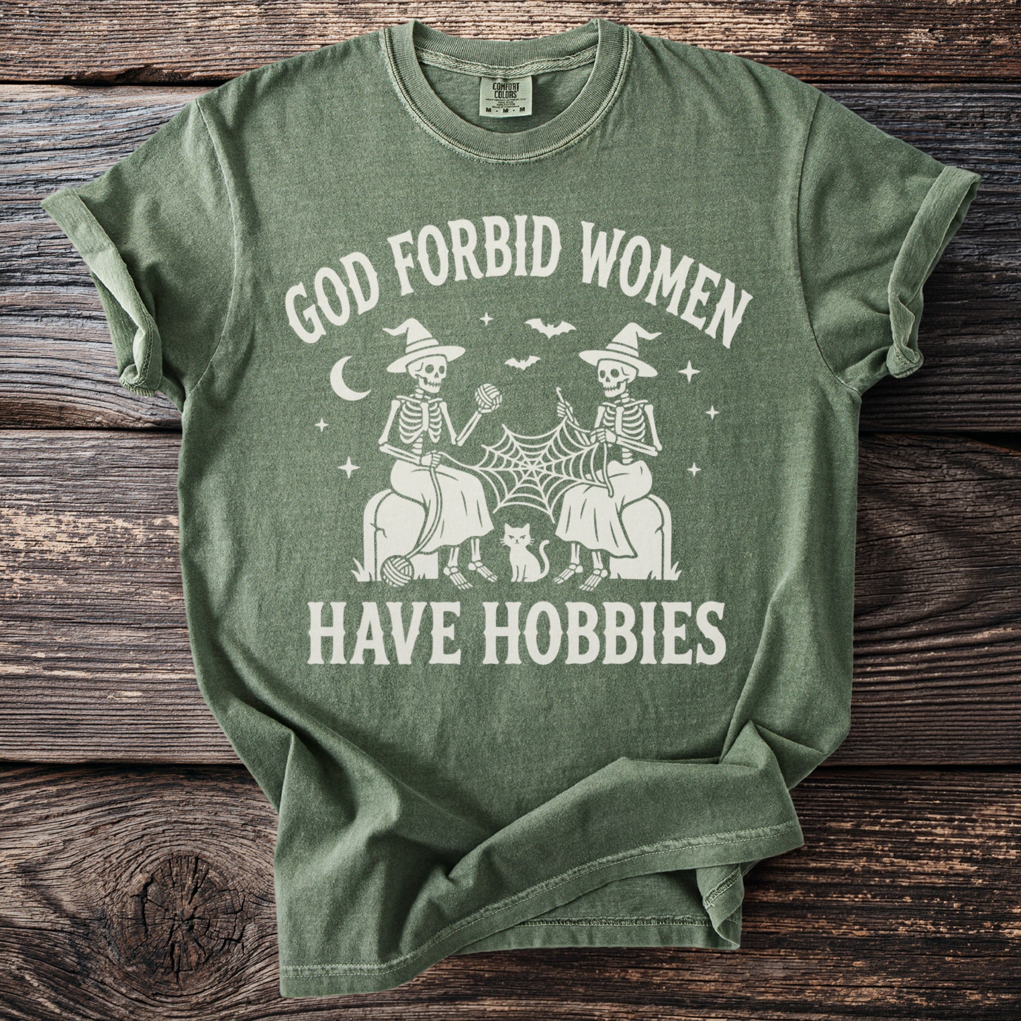 Green t-shirt with "God Forbid Women Have Hobbies" text and skeleton knitters.