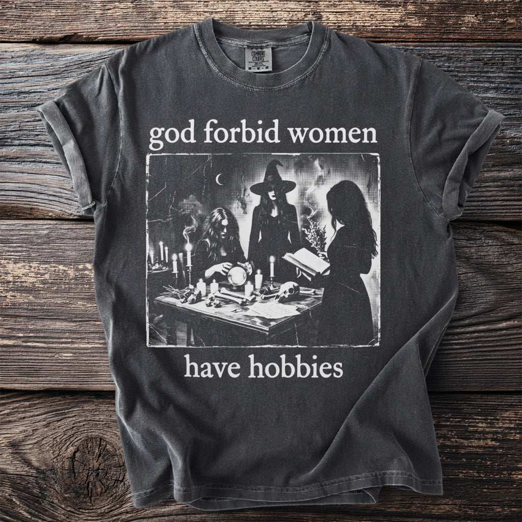 Dark gray t-shirt with the text "god forbid women have hobbies" and a graphic of witches.