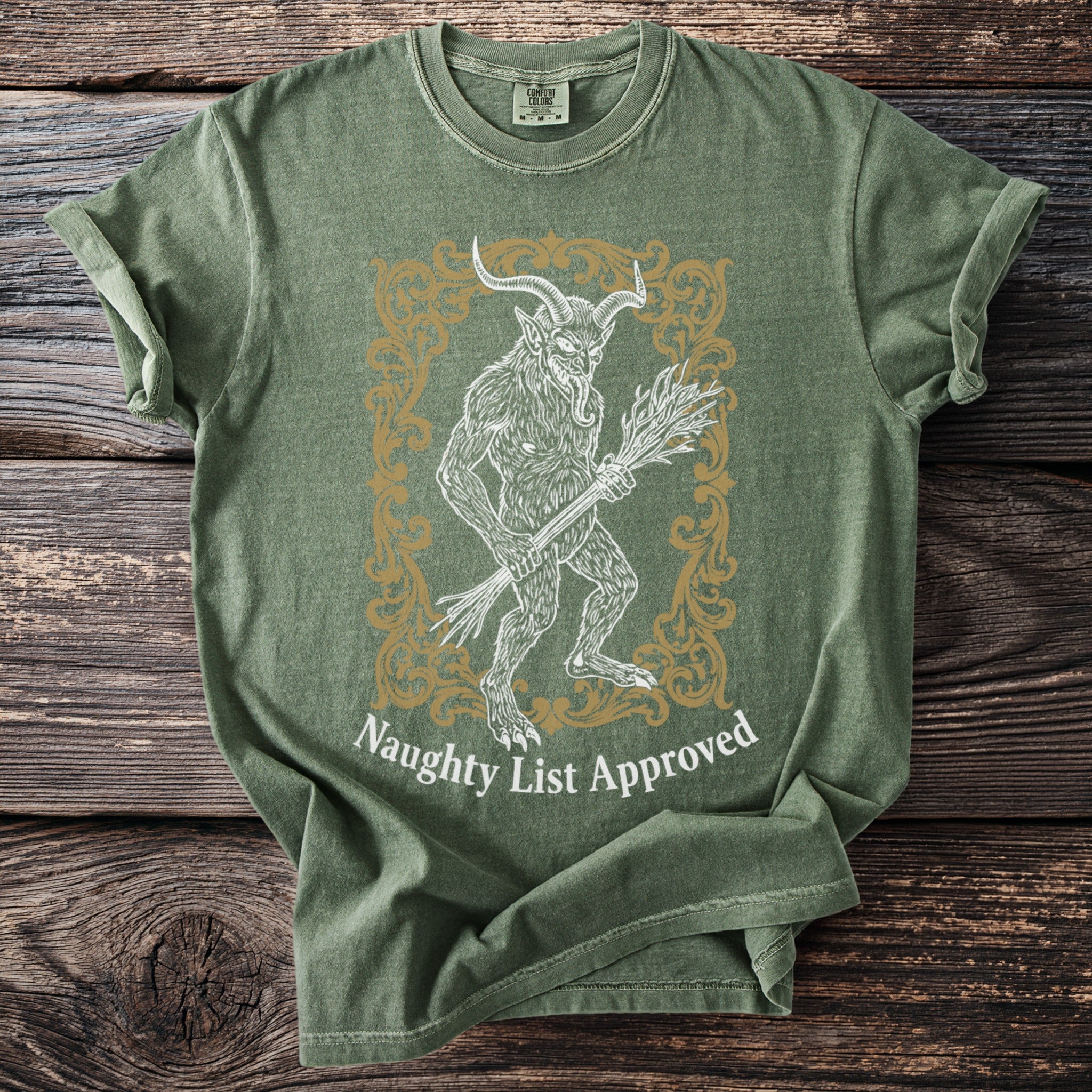 Green t-shirt with demon figure holding birch branches and text "Naughty List Approved."