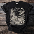 Black t-shirt with a cream graphic of a cat reading an open book with mystical symbols.