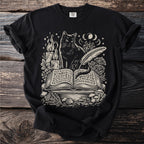 Black t-shirt with a cream graphic of a cat reading an open book with mystical symbols.
