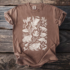 Brown t-shirt with an all-over illustration of various frogs, tadpoles, and aquatic plants.