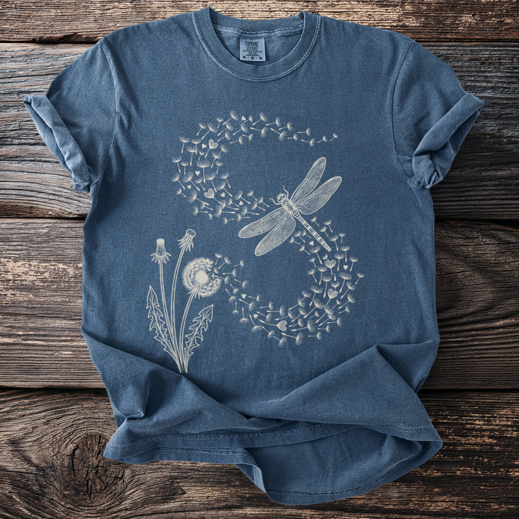 Blue t-shirt with a white graphic of a dragonfly flying from dandelion seeds.