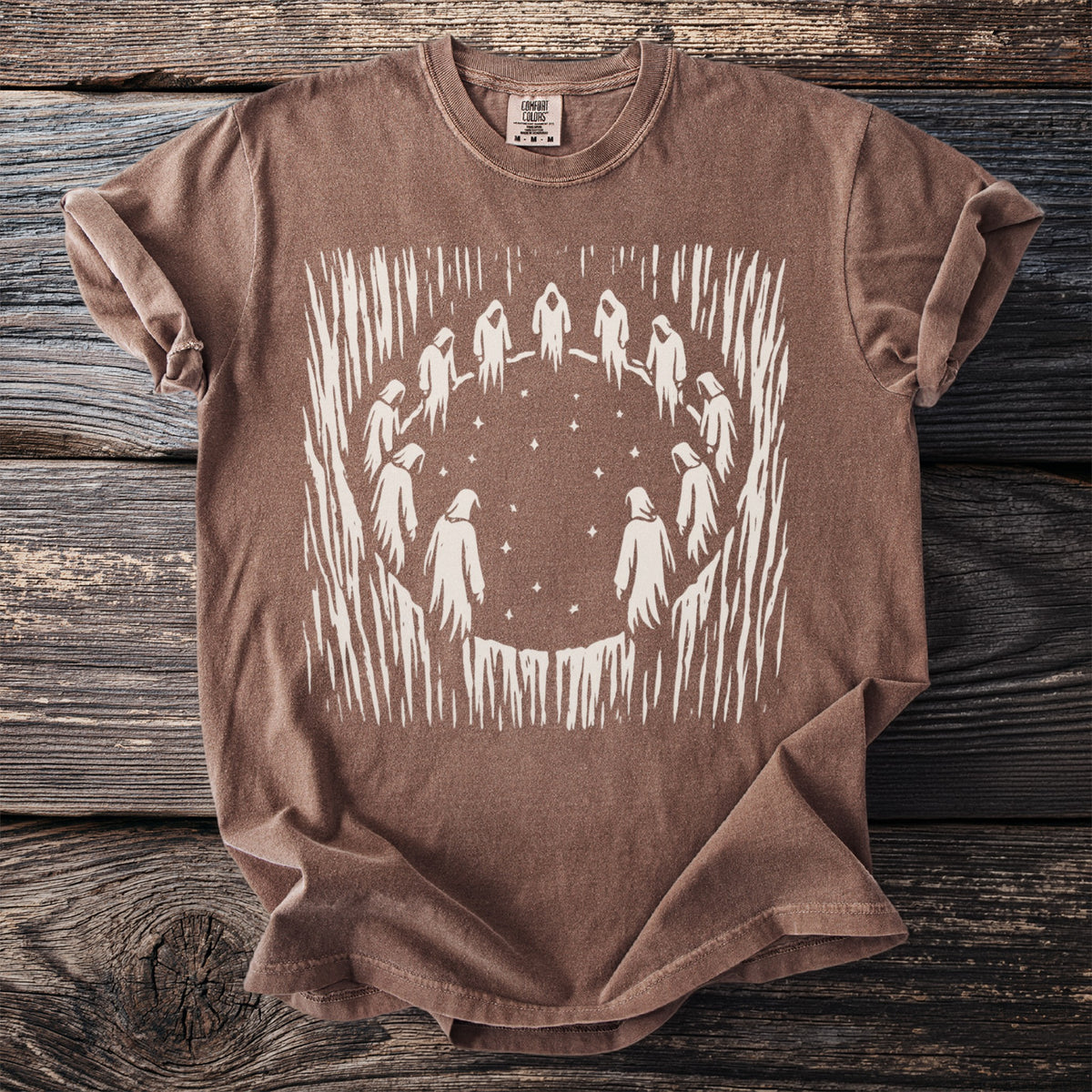 Brown t-shirt with a white circular design of cloaked figures and stars.