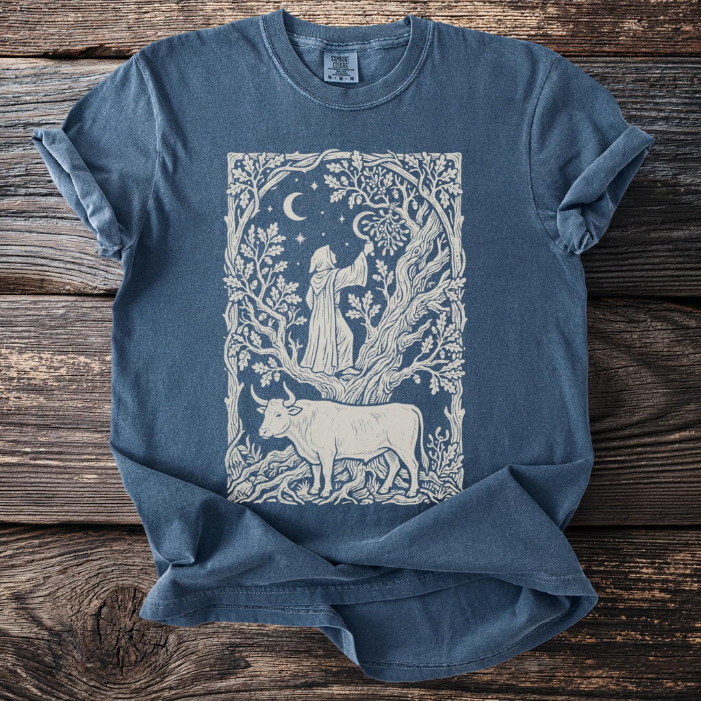 Blue t-shirt with a cream line art graphic of a hooded figure and a bull in a forest scene.