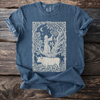 Blue t-shirt with a cream line art graphic of a hooded figure and a bull in a forest scene.