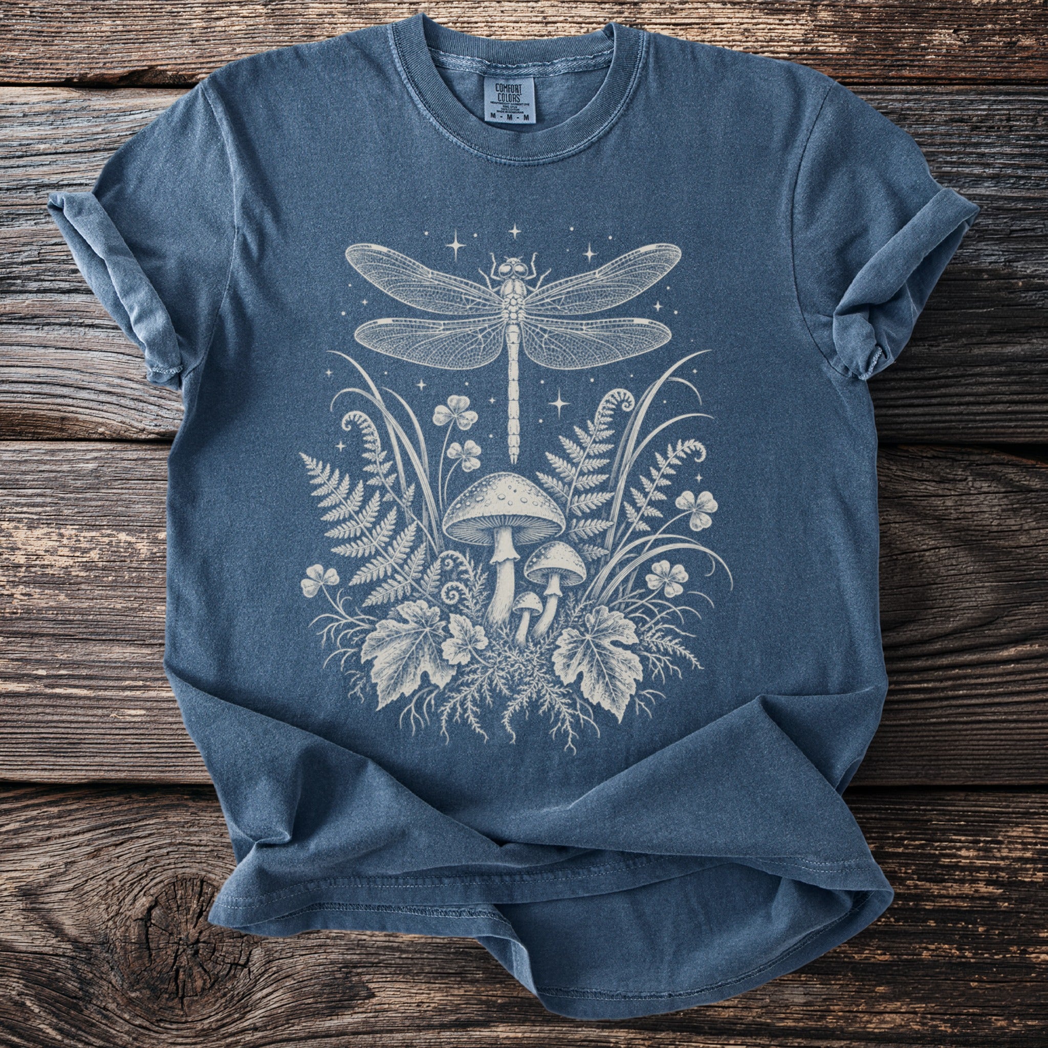 Blue t-shirt with dragonfly, mushrooms, and ferns graphic artwork.