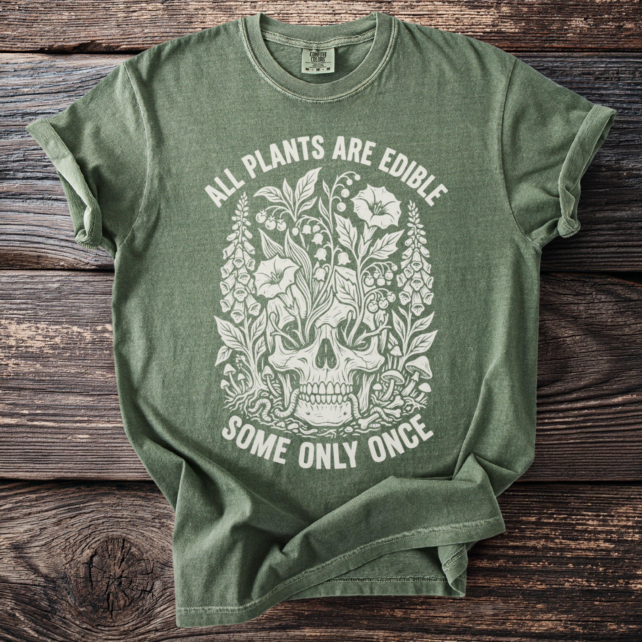Green t-shirt with a white graphic of a skull surrounded by plants and the text "ALL PLANTS ARE EDIBLE SOME ONLY ONCE".