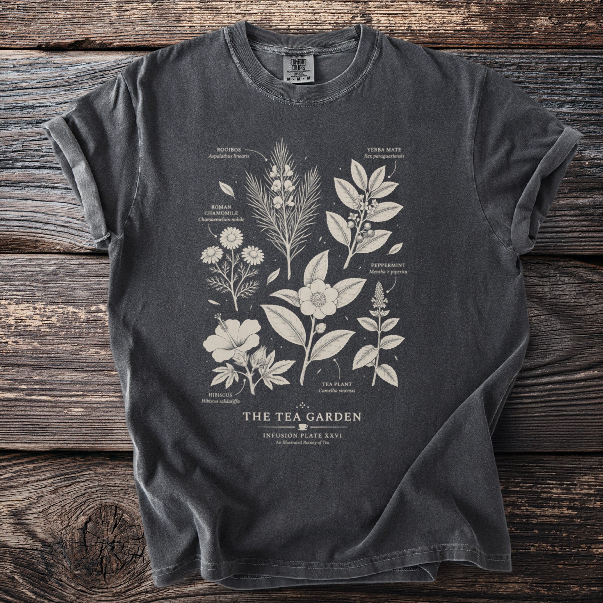 Gray t-shirt with "The Tea Garden" text and botanical illustrations of tea ingredients.