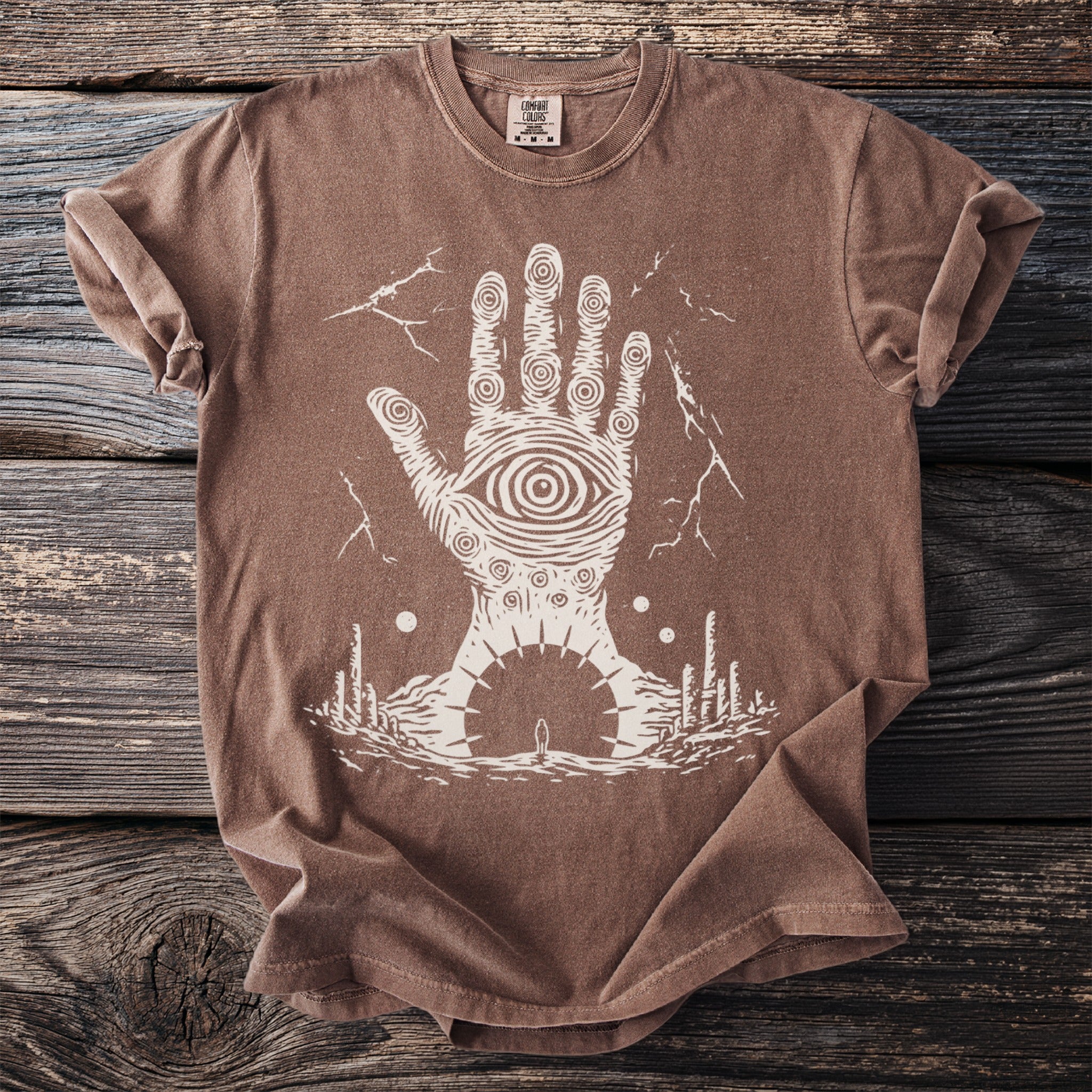 Brown t-shirt with a white graphic of a hand with an eye on its palm.