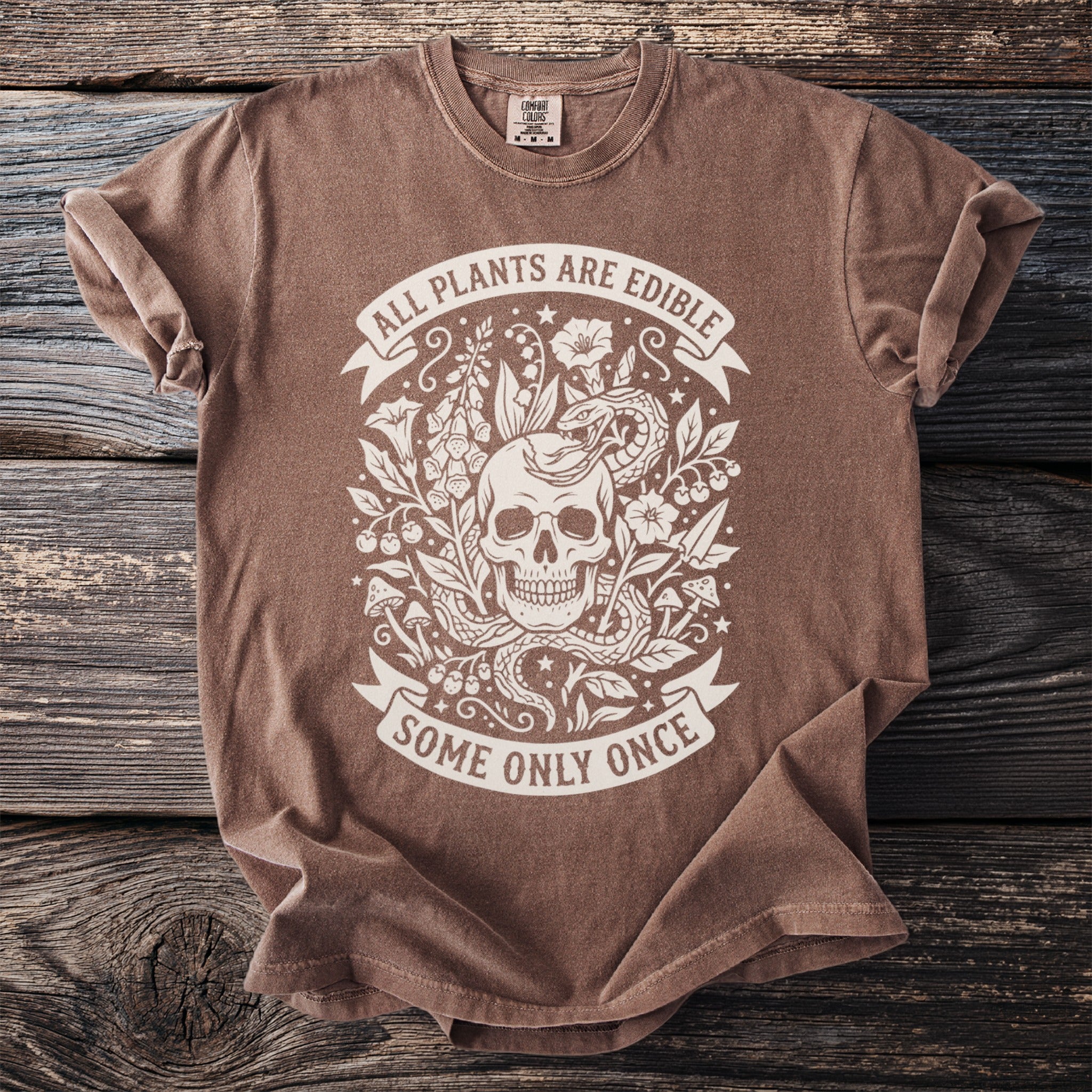 Brown t-shirt with skull, snake, and plants graphic and text "ALL PLANTS ARE EDIBLE SOME ONLY ONCE".