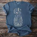 Blue t-shirt with a cream graphic of a witch in flames and occult symbols.