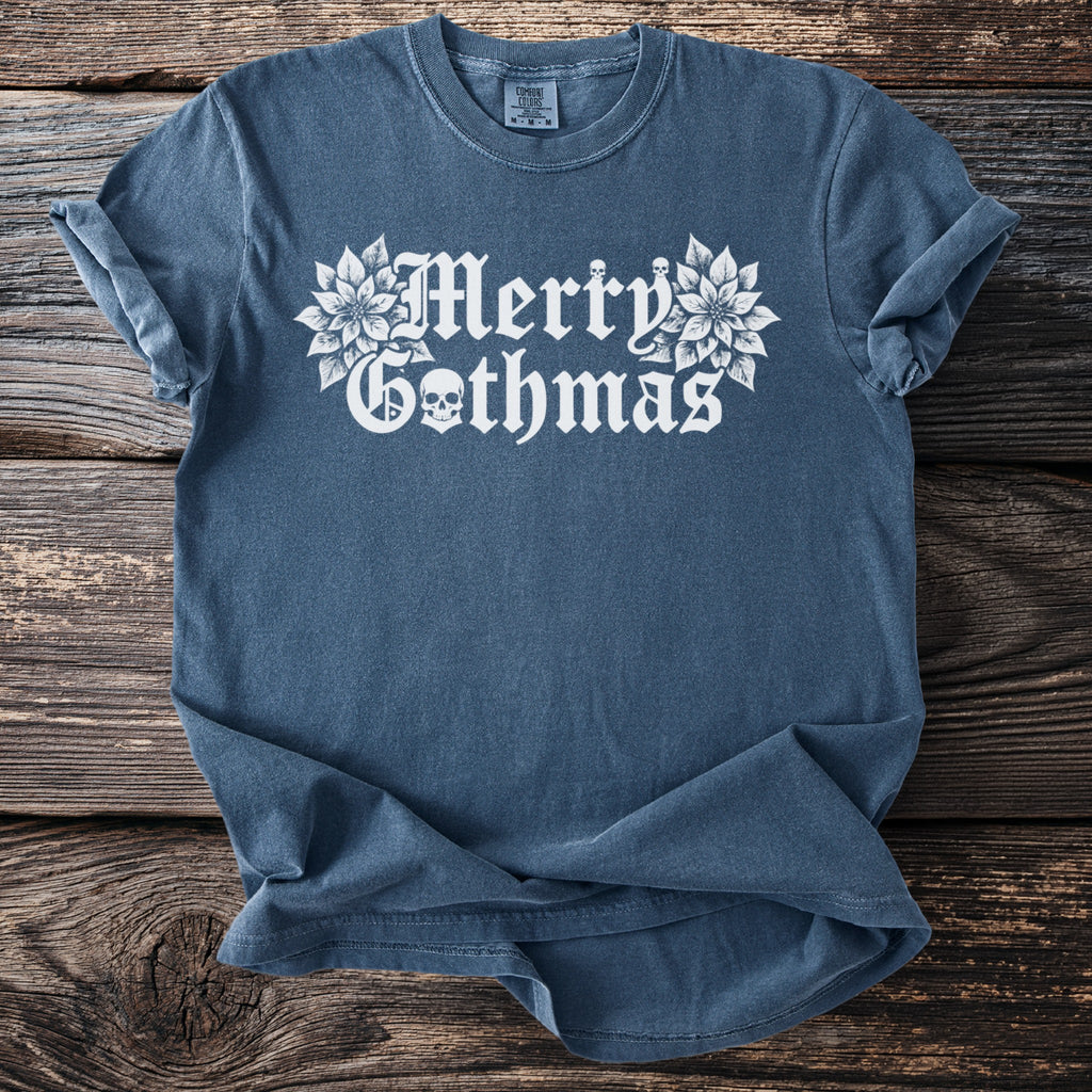 Blue t-shirt with white "Merry Gothmas" text and skulls on a wooden background