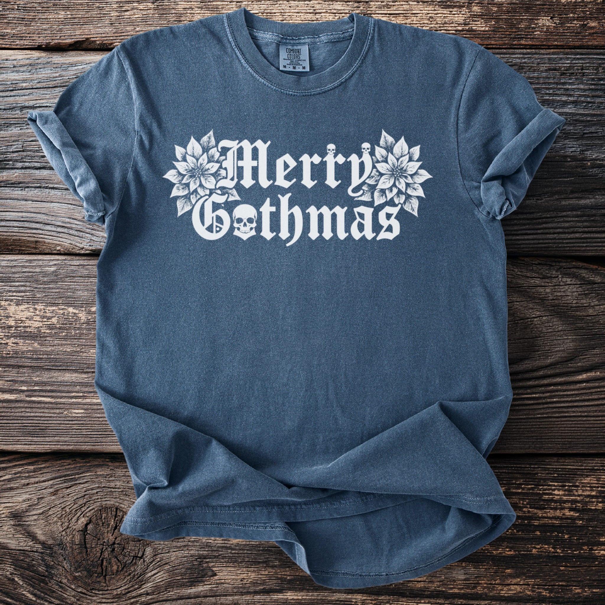 Blue t-shirt with white "Merry Gothmas" text and skulls on a wooden background