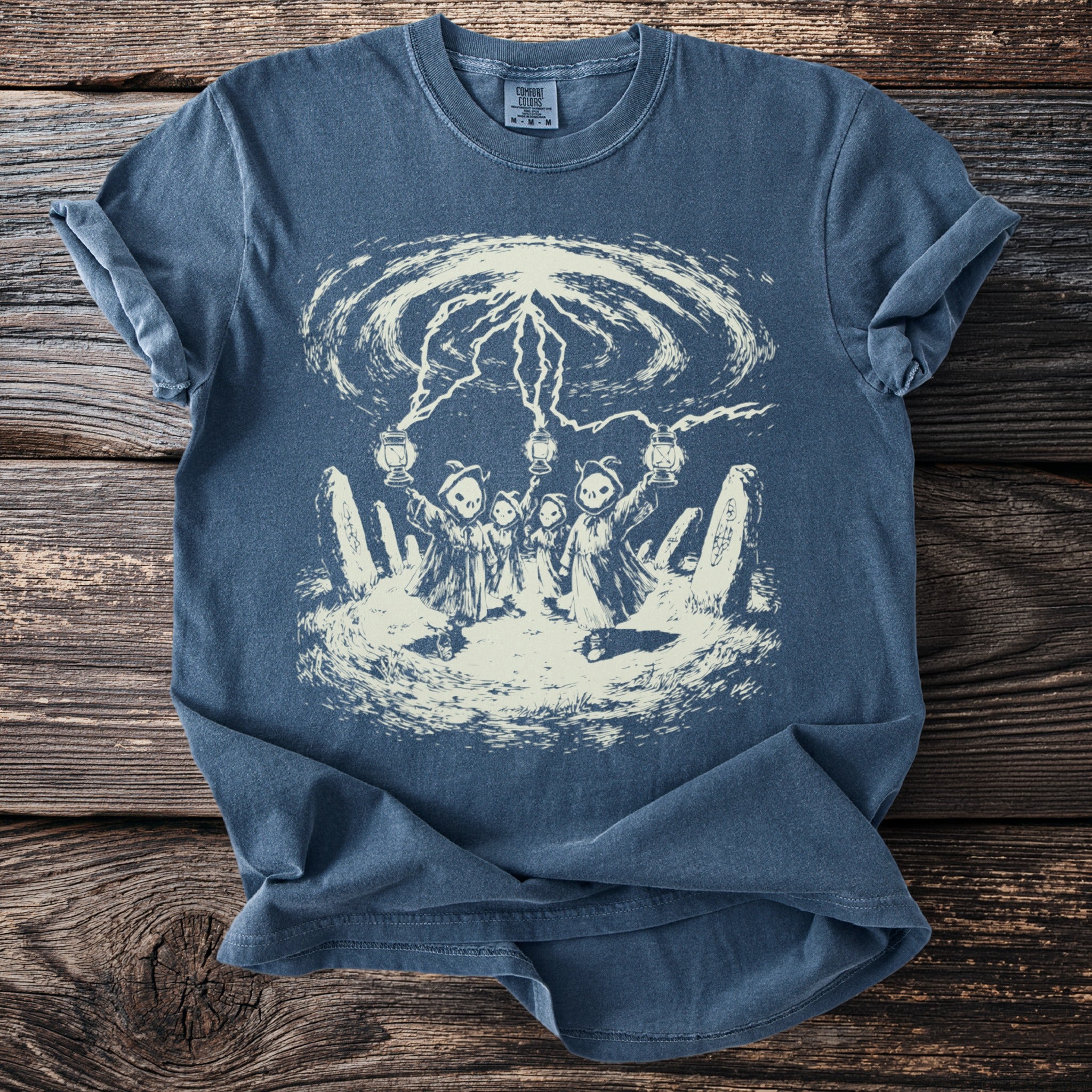 Blue t-shirt with a cream graphic of hooded figures holding lanterns under lightning bolts.