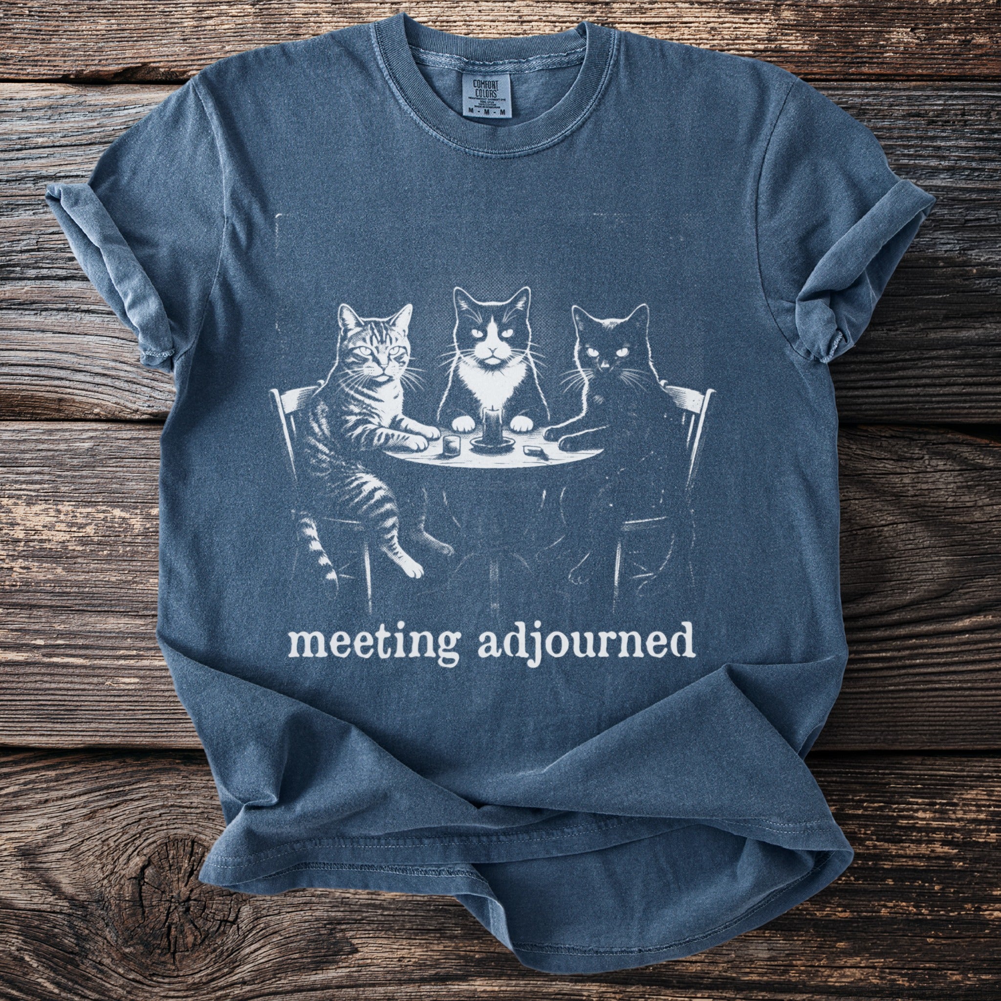 Blue t-shirt with graphic of three cats at a table, text "meeting adjourned"