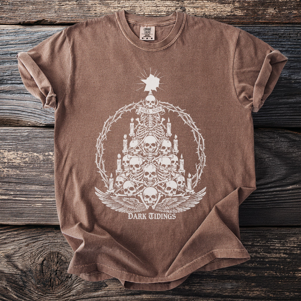 Brown t-shirt with a white graphic of a skull-and-bones Christmas tree and "DARK TIDINGS" text.