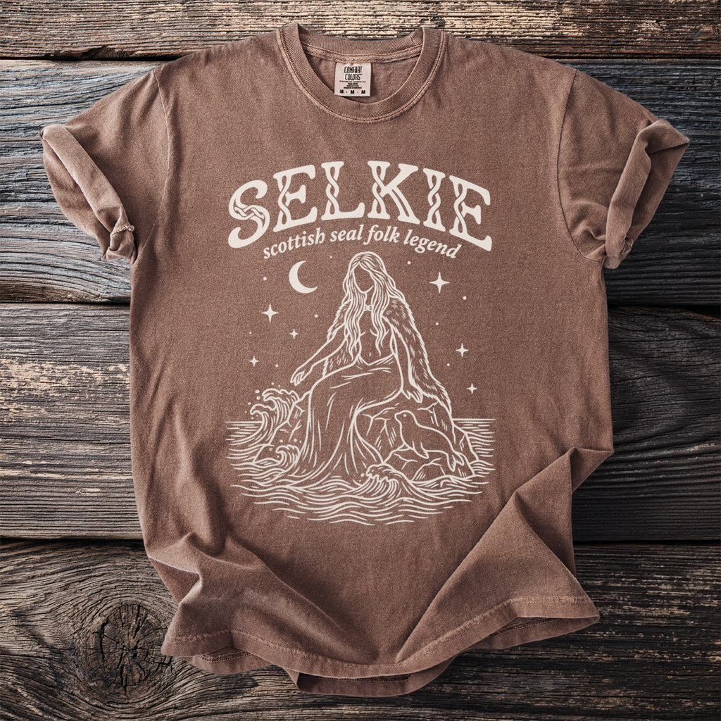Brown t-shirt with white "SELKIE scottish seal folk legend" and mythical creature design.