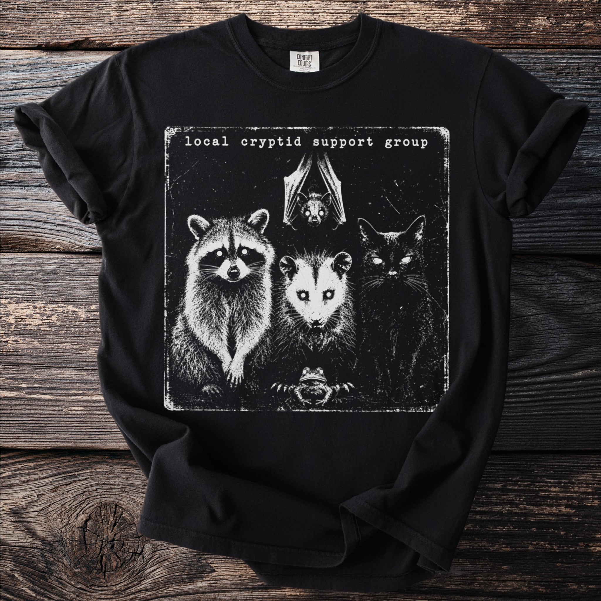 Black t-shirt with a graphic of a raccoon, opossum, cat, bat, and frog with white eyes.
