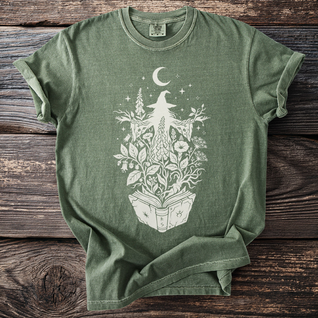 Green t-shirt with white witch and floral design emerging from an open book.