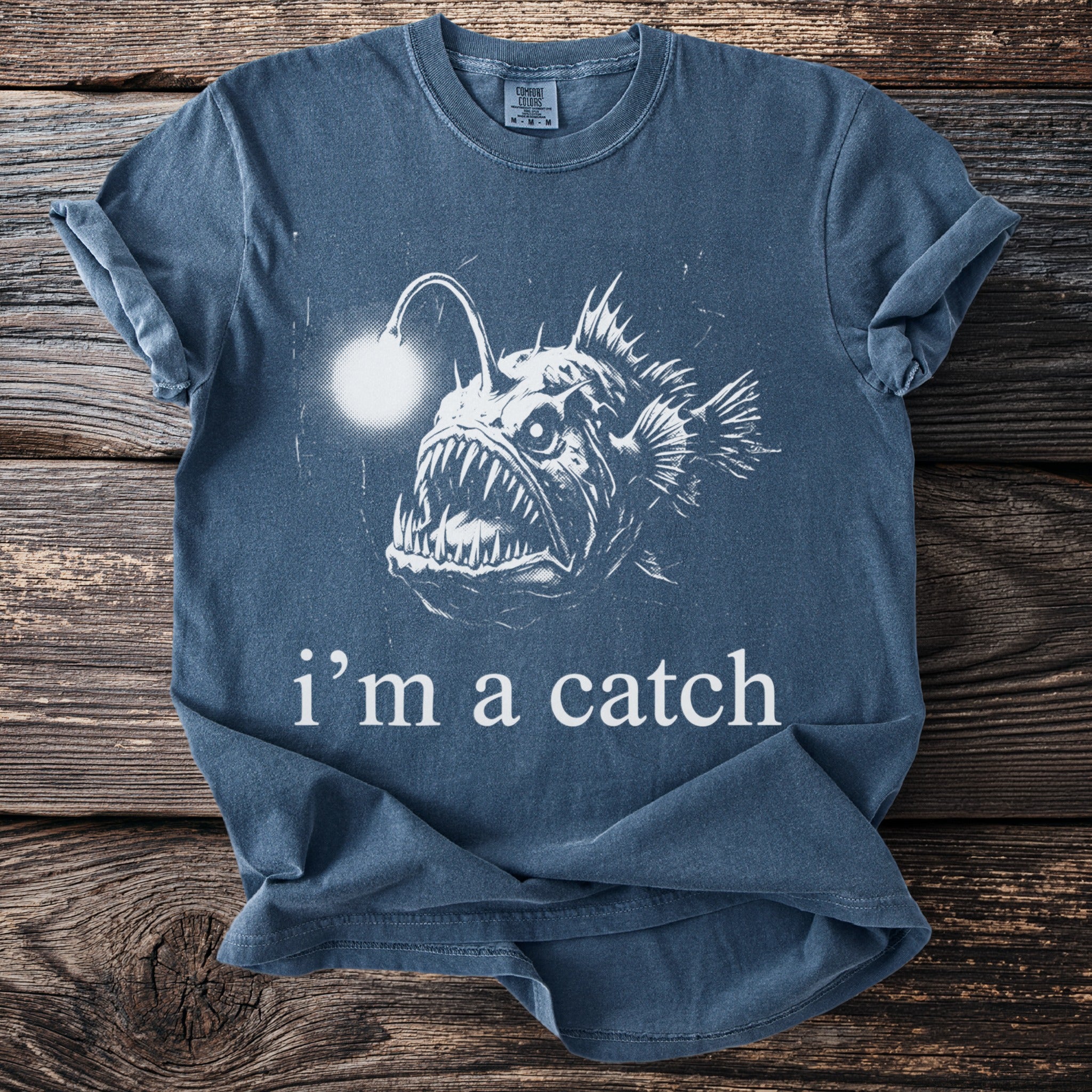 Blue t-shirt with a graphic of an anglerfish and text that reads "i'm a catch".