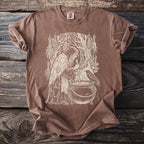 Brown t-shirt with a cream graphic of a witch stirring a cauldron with a raven.