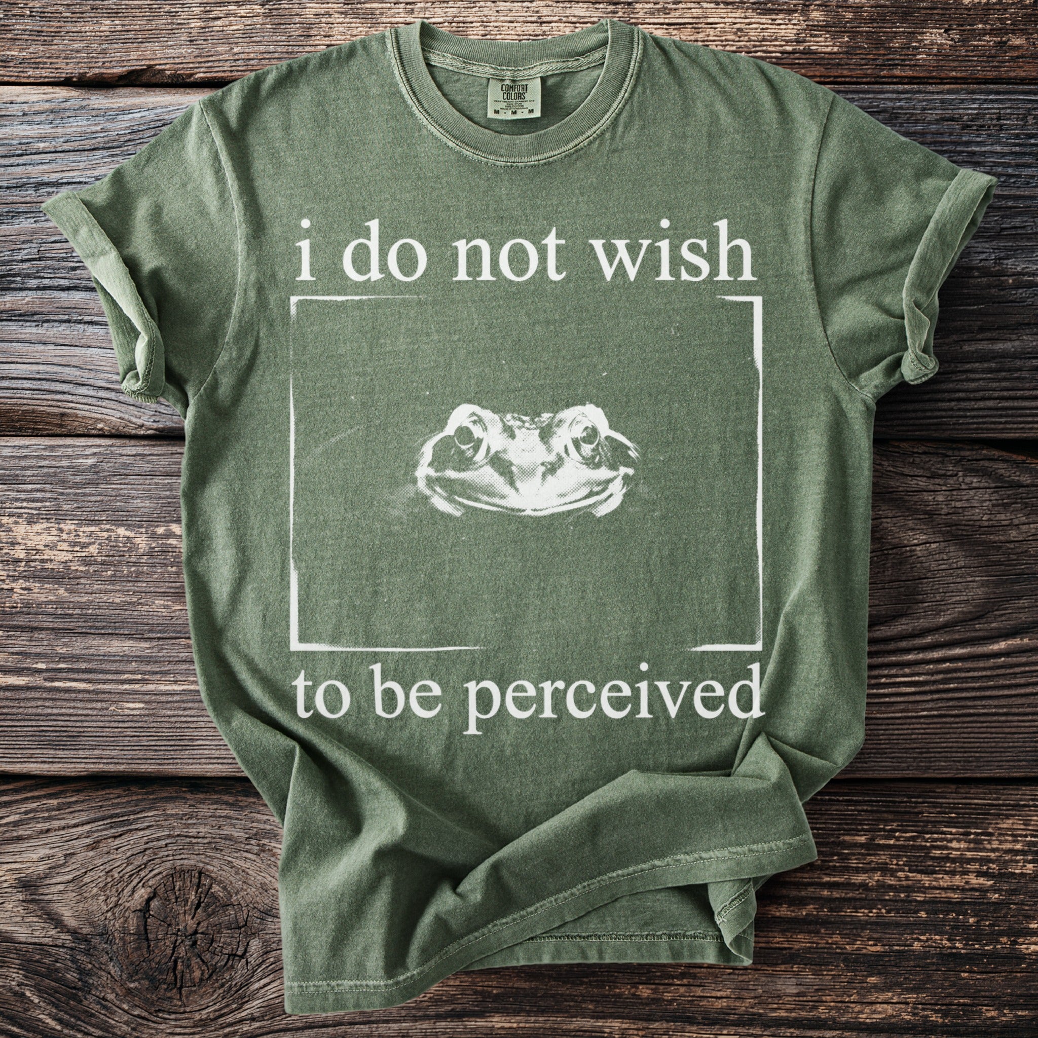 Green t-shirt with "i do not wish to be perceived" and a frog's head in a box.