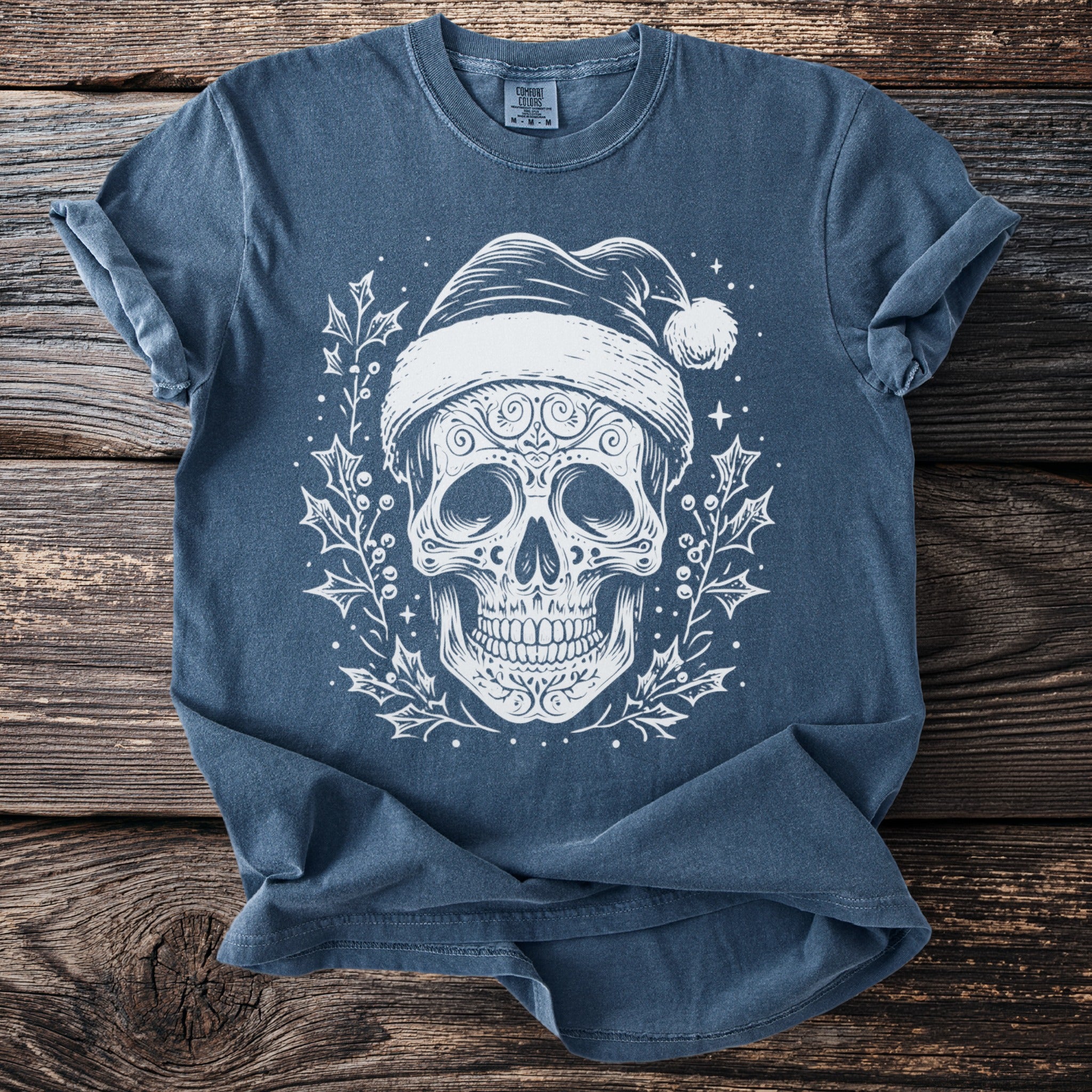 Blue t-shirt with a white graphic of a sugar skull wearing a Santa hat and surrounded by holly.
