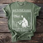 Green t-shirt with "god forbid women have hobbies" text and a woman with a basket graphic.