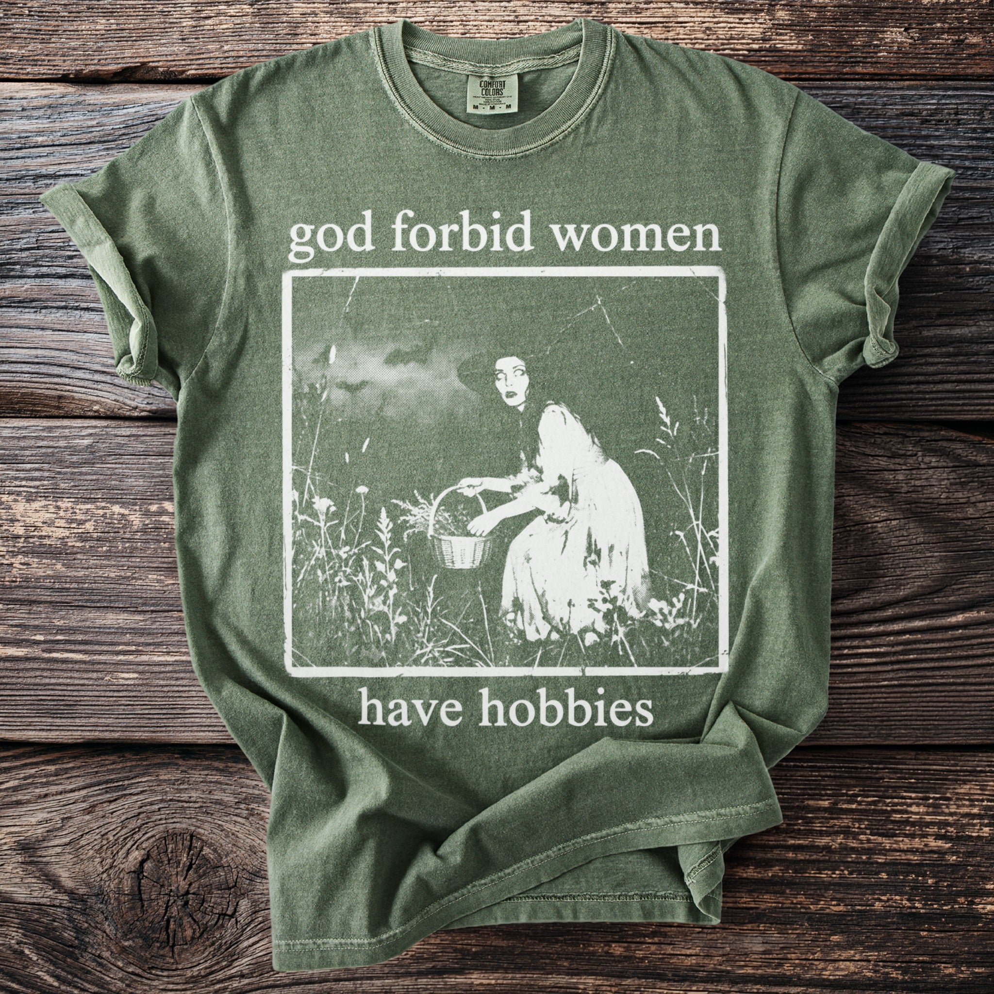 Green t-shirt with "god forbid women have hobbies" text and a woman with a basket graphic.