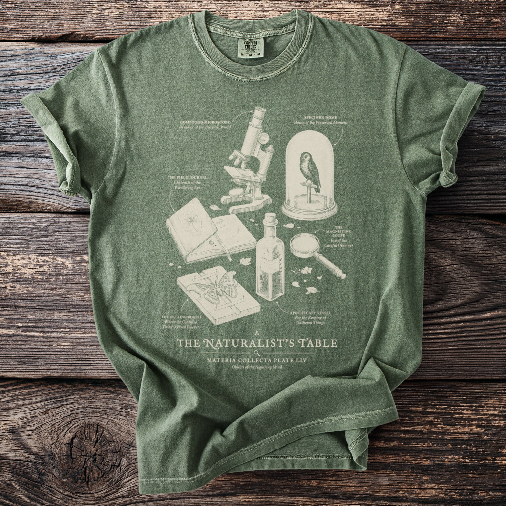 Green t-shirt with "The Naturalist's Table" graphic featuring a microscope, owl, and specimen board.