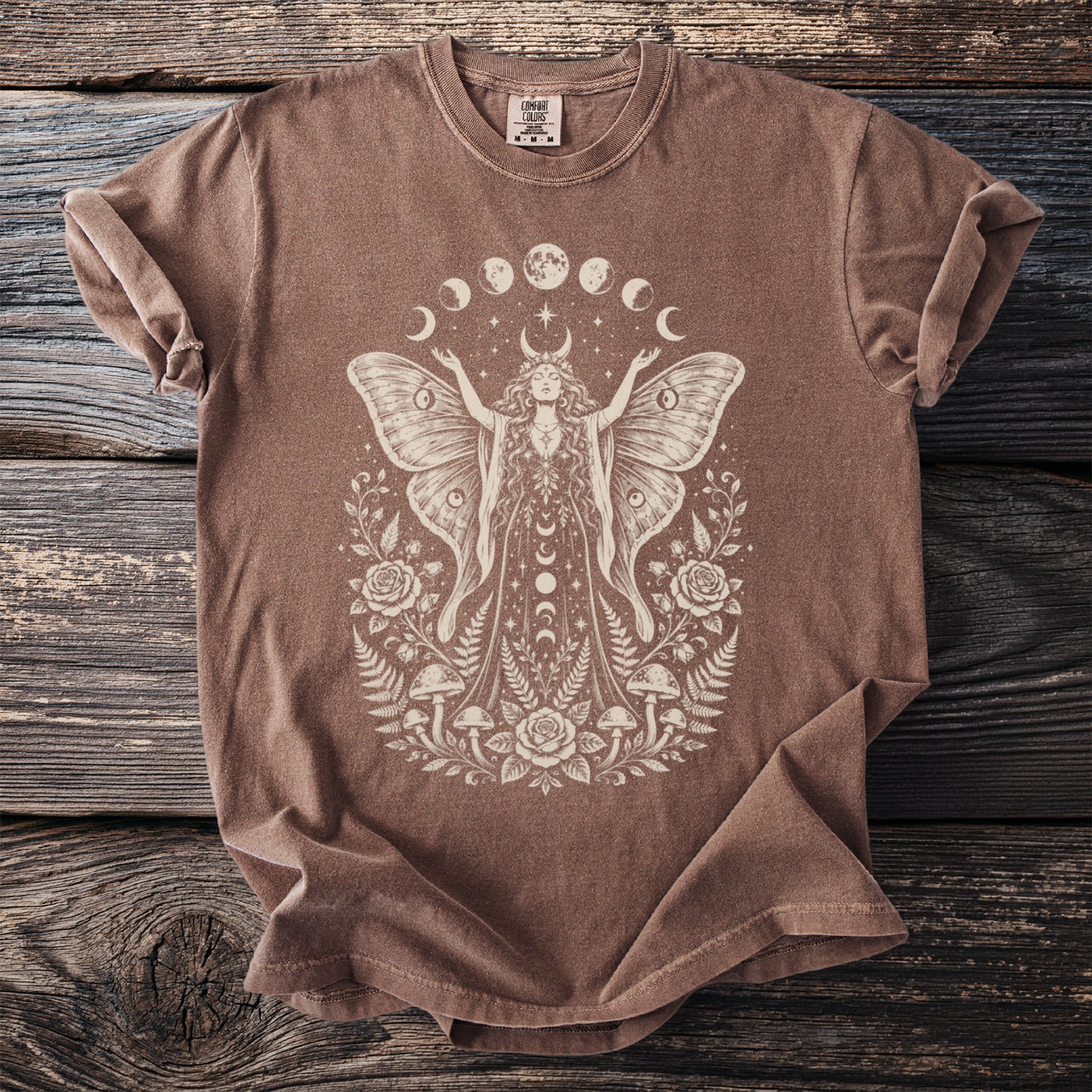 Brown t-shirt with a cream graphic of a moth woman surrounded by moons, roses, and mushrooms.