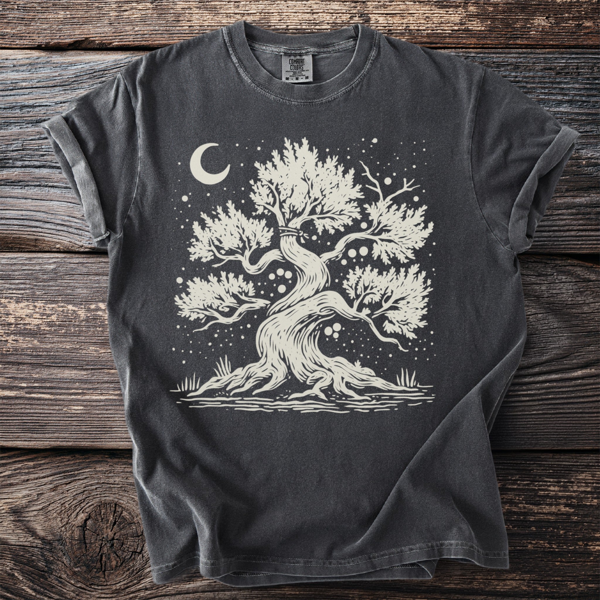 Dark t-shirt with a cream graphic of a stylized tree under a crescent moon and starry sky.